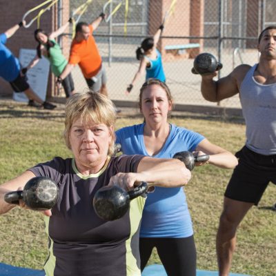 Mature woman and group exercising in outdoor boot camp fitness class